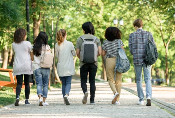 Group of teens walking together down a sidewalk away from camera.