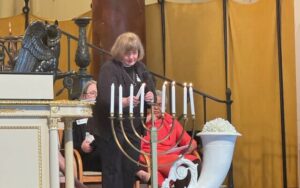 The Rev. Patricia Templeton lighting candle on menorah.